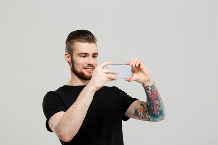 Young handsome man looking at phone, smiling over grey background.  Copy space.