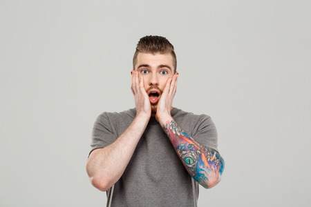 Surprised young handsome man posing, looking at camera over grey background. Copy space.の写真素材