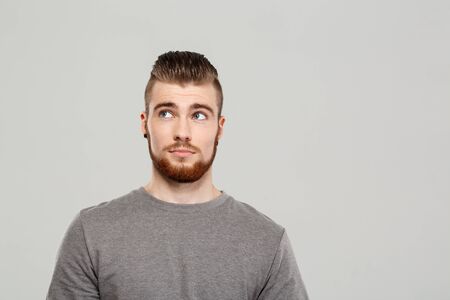 Young handsome man posing, looking in side over grey background. Copy space.の写真素材