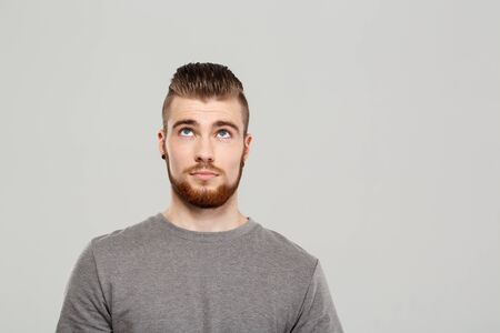 Young handsome man posing, looking up over grey background. Copy space.