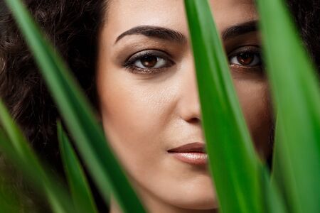 Young beautiful brunette girl in tropical plants looking at camera, smiling over grey background.の写真素材