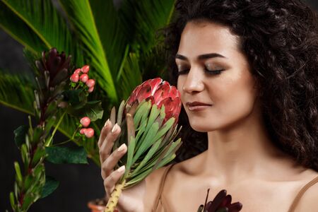 Young beautiful brunette girl in tropical plants smiling with closed eyes over grey background.の写真素材
