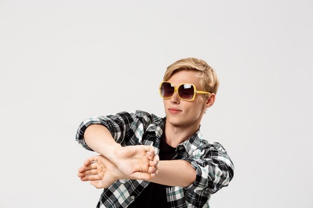 Funny blond handsome young man wearing sunglasses and casual plaid shirt dancing, copy space, grey backgroundの写真素材