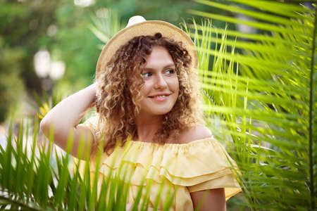 Young beautiful girl in yellow dress and hat smiling, posing in city park.の写真素材