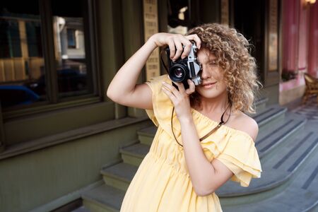 Young beautiful photographer in yellow dress smiling, walking around city.