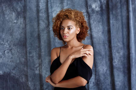 Young beautiful african girl posing over grey cloth background. Copy space.の写真素材