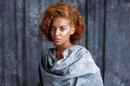 Young beautiful african girl looking at camera, posing, wrapping up  in grey cloth. Copy space.の写真素材