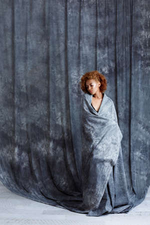 Young beautiful african girl posing, wrapping up  in grey cloth. Copy space.の写真素材
