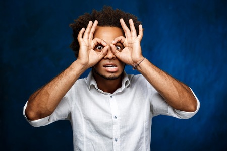 Young handsome african man in white shirt posing over blue background. Copy space.の写真素材