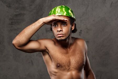Young handsome frican man with watermelon on head fooling over grey background. Copy space.の写真素材
