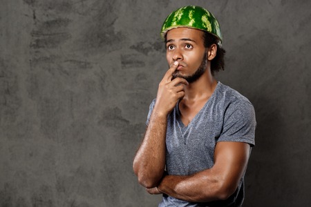 Young handsome frican man with watermelon on head fooling over grey background. Copy space.の写真素材