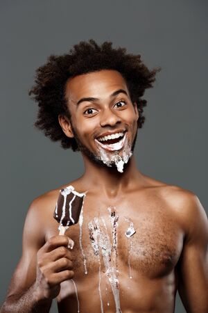 Young handsome african man eating icecream, posing over grey background. Copy space.の写真素材