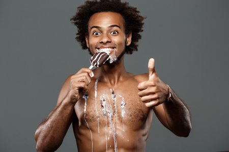 Young handsome african man eating icecream, posing over grey background. Copy space.の写真素材