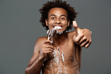 Young handsome african man eating icecream, posing over grey background. Copy space.の写真素材