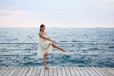 Young beautiful ballerina dancing and posing outside early in morning, sea background.の写真素材
