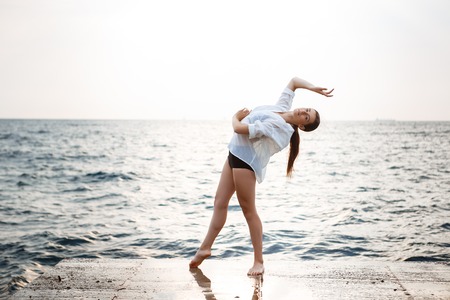 Young beautiful ballerina dancing and posing outside early in morning, sea background.の写真素材