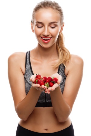 Young beautiful sportive girl posing, holding strawberries over white background. Copy space.の写真素材