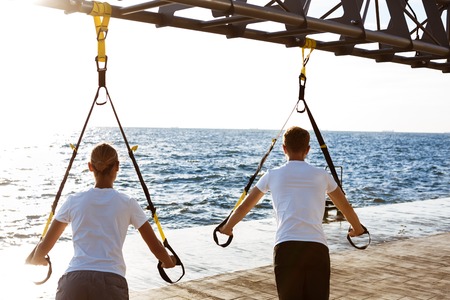 Young beautiful sportive people training with trx near sea.の写真素材