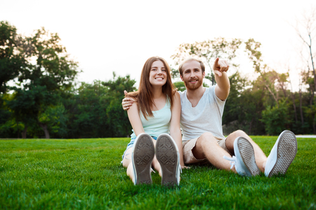 Young beautiful couple smiling, resting, sitting on grass in park.の写真素材