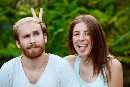 Young beautiful couple posing, smiling, showing tongue, walking in parkの写真素材