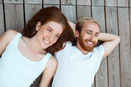 Young beautiful couple smiling, lying on wooden boards.の写真素材