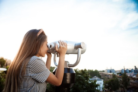 Young beautiful girl in sunglasses walking around city, looking through binoculars.
