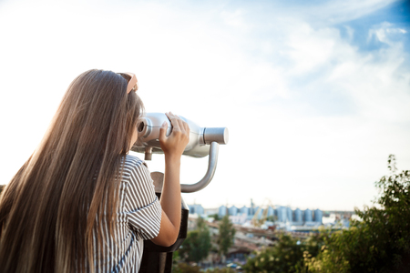 Young beautiful girl in sunglasses walking around city, looking through binoculars.の写真素材