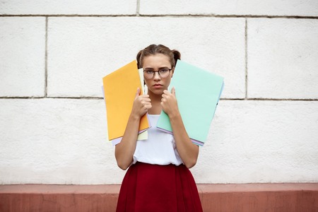 Upset young beautiful female student  holding folders outdoors.の写真素材