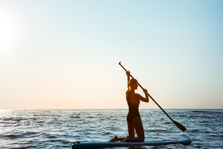 Silhouette of young beautiful girl surfing in sea at sunrise. Outdoors.の写真素材