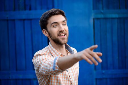 Young handsome man smiling, pointing finger away over blue background.の写真素材