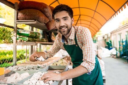 Young handsome gardener smiling, preparing planting flowers.の写真素材