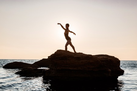 Young beautiful ballerina dancing, posing on rock at beach, sea background.の写真素材