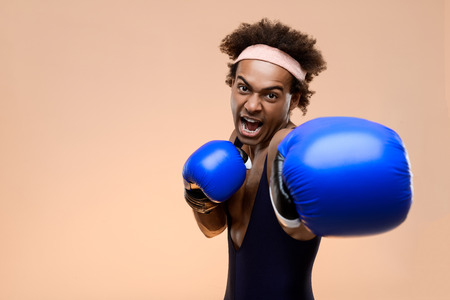 Young handsome sportive african man in boxing gloves training over orange background. Copy space.