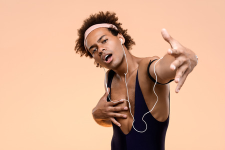 Young handsome sportive african man listening music in headphones, singing over orange background. Copy space.の写真素材