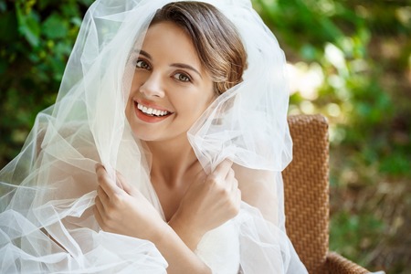 Young beautiful blonde bride in wedding dress and veil smiling, looking at camera. Copy space.の写真素材