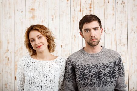 Young beautiful couple looking at camera over wooden background. Girl smiling, man sad. Copy space.の写真素材