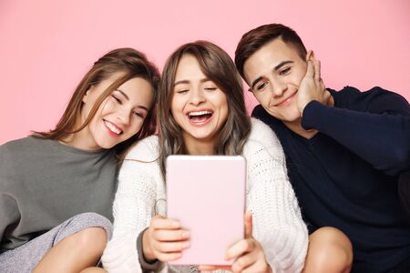 Young beautiful friends smiling making selfie on tablet over pink background.の写真素材