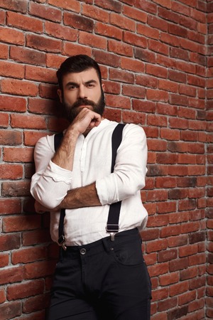 Young handsome man in suit with suspenders thinking posing over brick background. Copy space.の写真素材