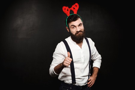 Young handsome man in fake deer horns showing okay over black background. Copy space.の写真素材