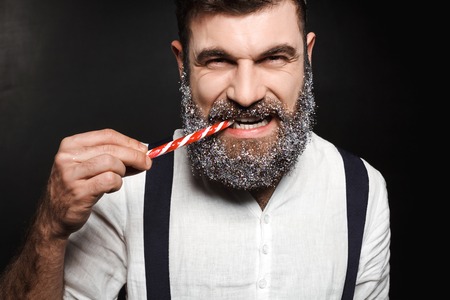 Young handsome man eating christmas candy over black background. Copy space.の写真素材