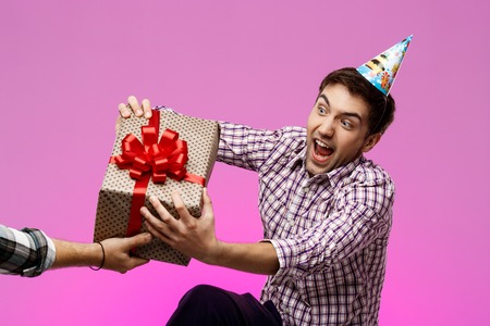 Young handsome man tearing out birthday gift in box over purple background. Copy space.の写真素材