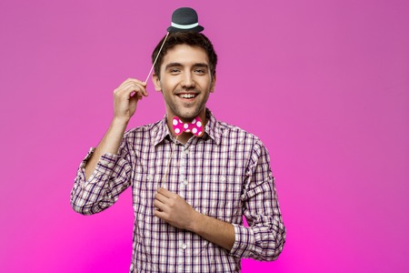 Young handsome man wearing fake hat and butterfly over purple background. Copy space.の写真素材