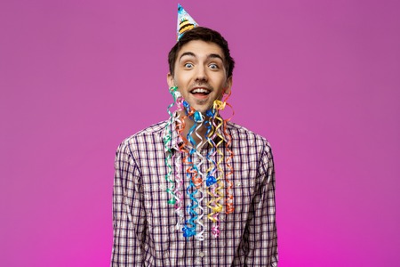 Surprised young man with fake beard smiling at birthday party over purple background. Copy space.の写真素材