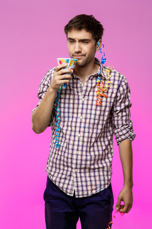 Displeased tired man at birthday party over purple background. Copy space.の写真素材