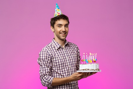 Young handsome man smiling, holding birthday cake over purple background. Copy space.の写真素材