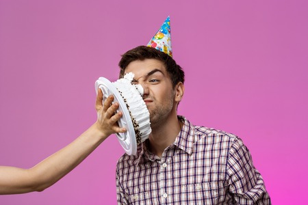 Young handsome man with cake on face over purple background. Birthday party. Copy space.の写真素材