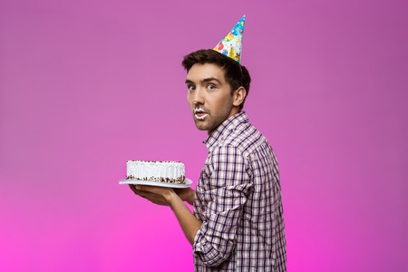 Young handsome man with cake on lips over purple background. Birthday party. Copy space.の写真素材