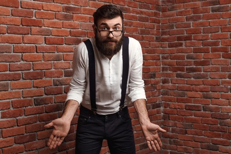 Young handsome man in suit with suspenders and glasses gesturing over brick background. Copy space.の写真素材