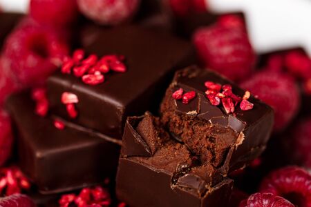 Chocolate candies and raspberry on white plate over sackcloth. Close up.