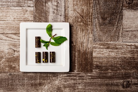 Chocolate candies and mint on white plate over wooden background. From above. Copy space.の写真素材